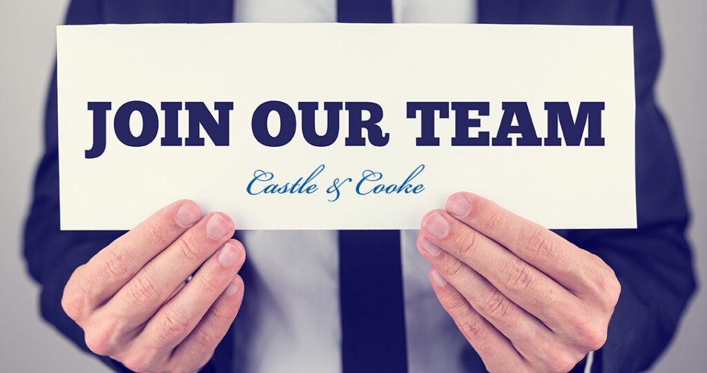 A person in a business suit holding a sign that reads "join our team" with the logo of castle & cooke, emphasizing a call for team recruitment.