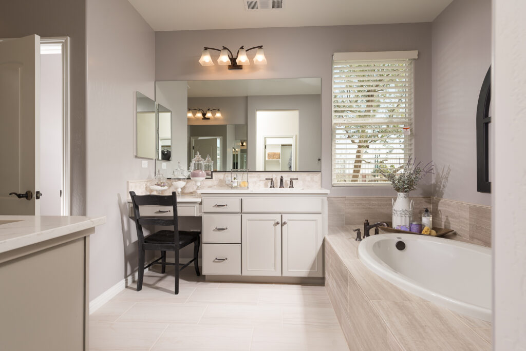 Elegant bathroom featuring a freestanding tub, his-and-hers sinks with large mirrors, white cabinetry, and a makeup vanity, illuminated by natural and artificial light.