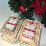 Two festive holiday meals packaged, labeled "happy holidays highgate - turkey with stuffing" and "chicken enchilada," displayed on a countertop with christmas decorations nearby.