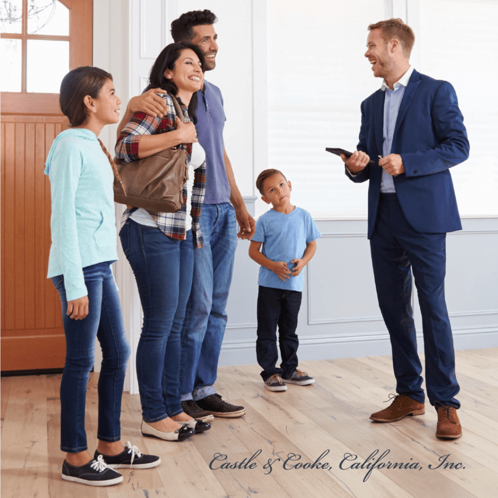 A family of four listens to a real estate agent in a bright, spacious room. the agent, dressed in a suit, gestures with his hand while the family stands engaged in conversation.