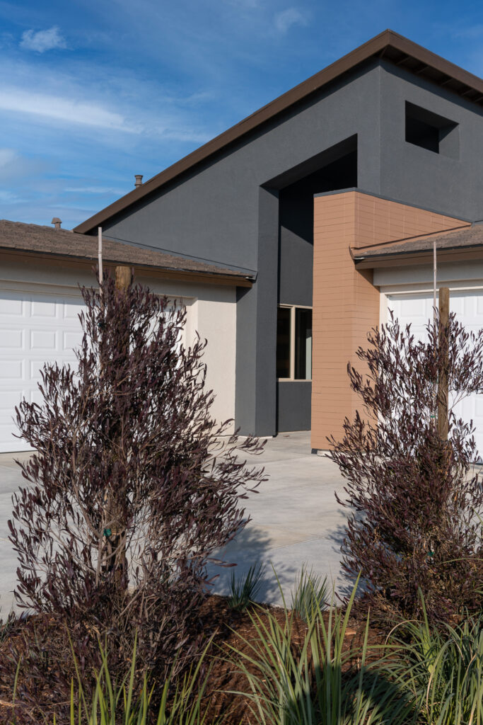 A modern house with a juxtaposition of dark gray and tan sections, featuring a clean, geometric design and complemented by drought-resistant landscaping in the foreground.