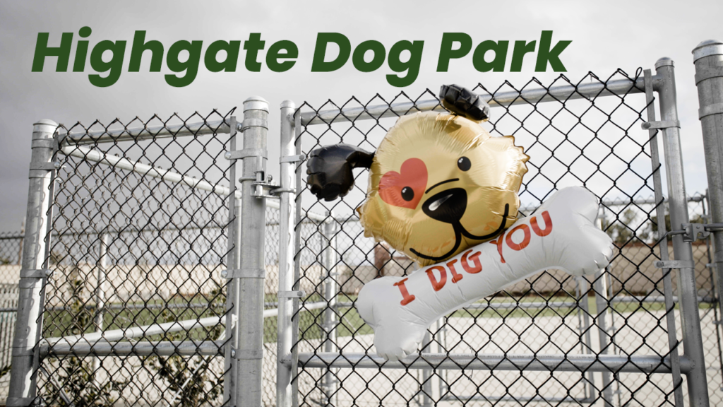 An inflatable dog-shaped balloon with "i dig you" text floats near the entrance of highgate dog park, which has a chain-link fence and overcast sky in the background.