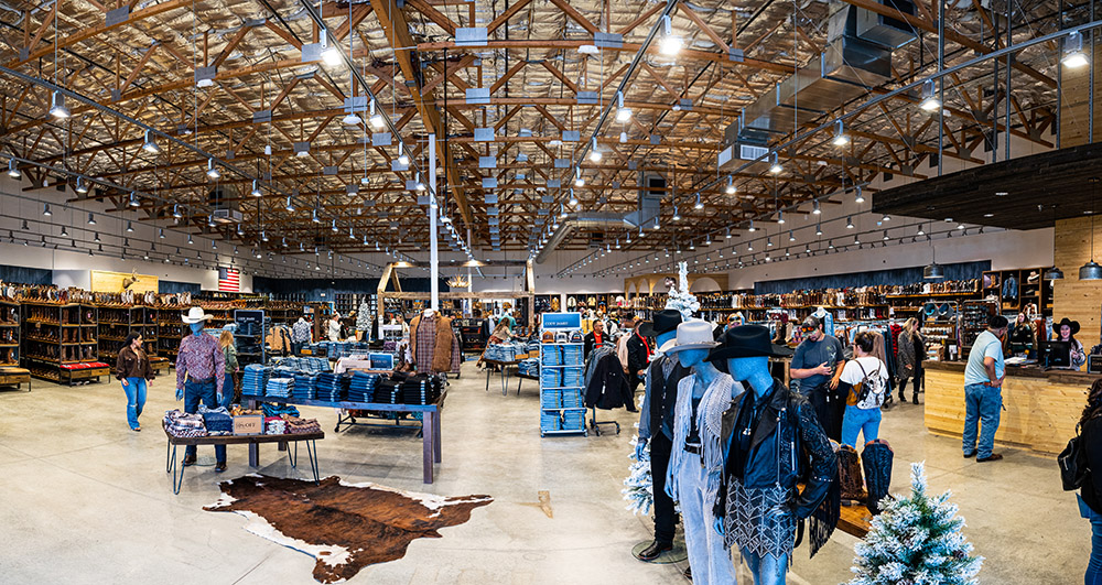 Wide interior view of a spacious clothing store with a rustic design, featuring wooden beams, various clothing racks, and shoppers browsing items.