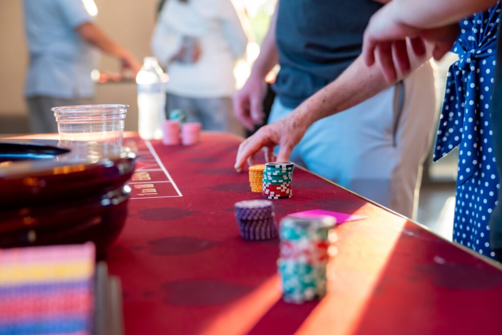 A person places a stack of multicolored poker chips on a casino table at a gaming event, with others around in a softly lit environment.