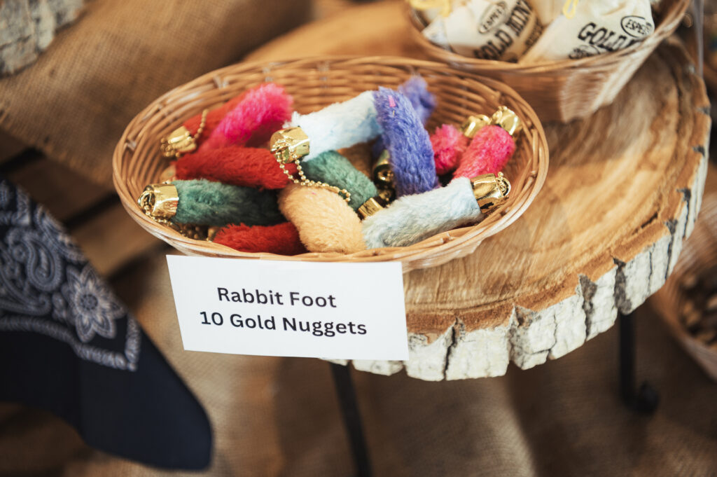 A wicker basket filled with colorful rabbit foot keychains on a wooden display. A sign in front reads, "Rabbit Foot 10 Gold Nuggets.