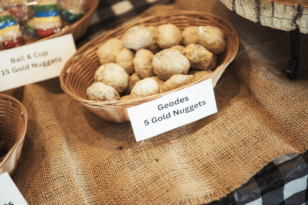 A basket filled with geodes is displayed on a burlap tablecloth. A sign in front reads, "Geodes 5 Gold Nuggets." Other baskets with labels are partially visible in the background.